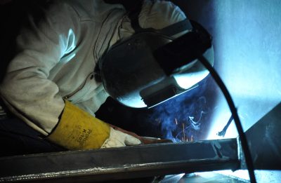 Welder bent and hunched over, working in a dark and cramped environment