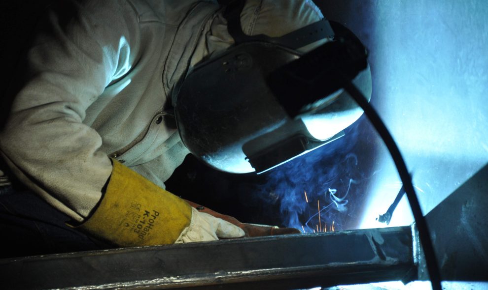 Welder bent and hunched over, working in a dark and cramped environment