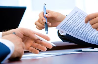Close-up of two workers working on a report together at a wooden table.