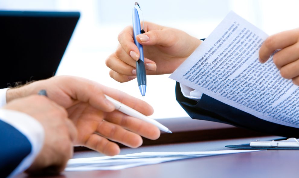 Close-up of two workers working on a report together at a wooden table.