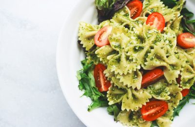 A bowl of pasta with a green sauce and salad.