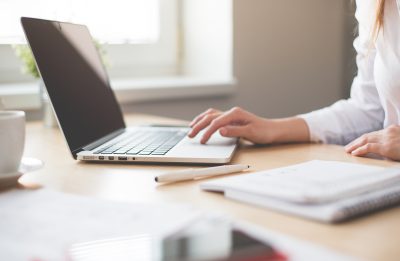 Female worker at her desk with an open laptop and notebook.